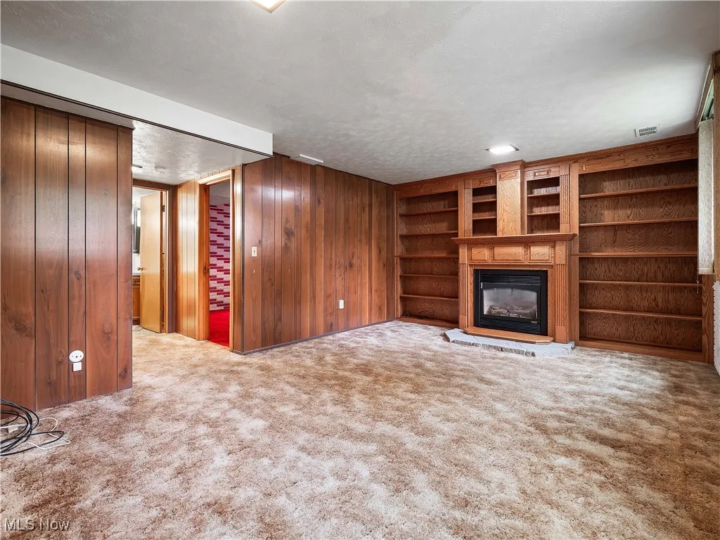 Unfurnished living room featuring wooden walls, a textured ceiling, light carpet, a glass covered fireplace, and built in features