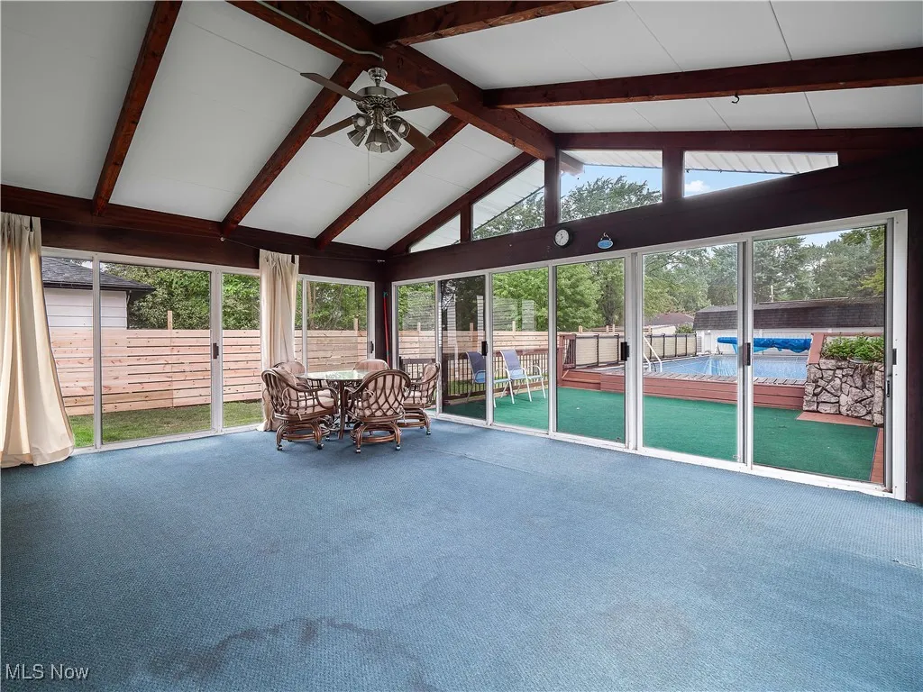 Sunroom / solarium featuring beamed ceiling, carpet flooring, and high vaulted ceiling