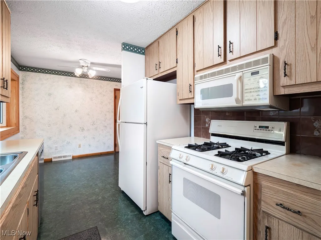 Kitchen featuring white appliances, wallpapered walls, light countertops, a textured ceiling, and backsplash