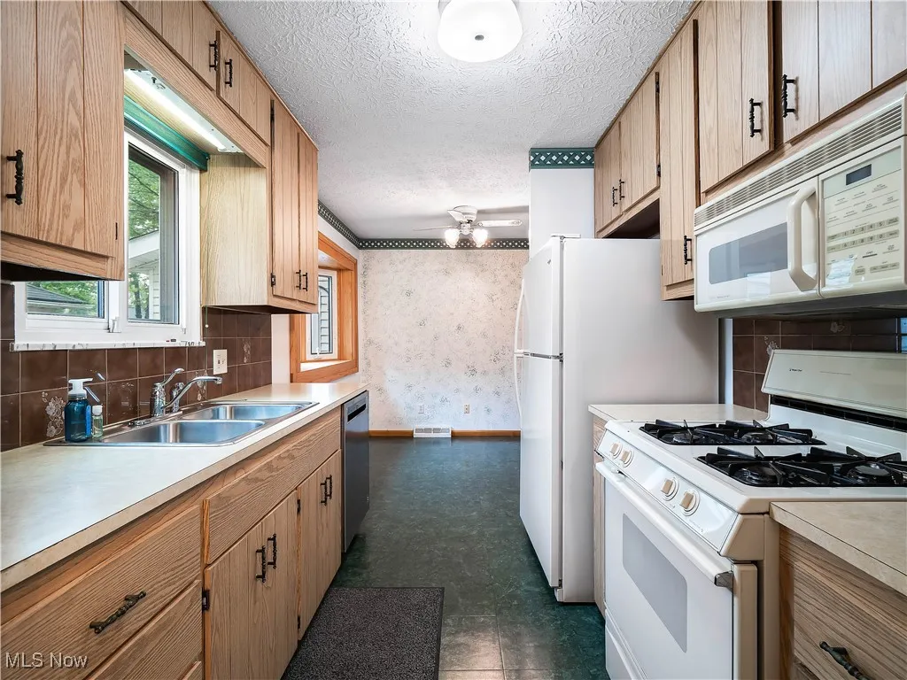 Kitchen featuring wallpapered walls, decorative backsplash, white appliances, light countertops, and a textured ceiling