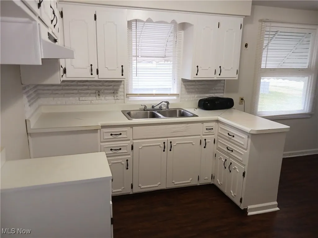 Kitchen featuring light countertops, white cabinets, dark wood-type flooring, under cabinet range hood, and a peninsula