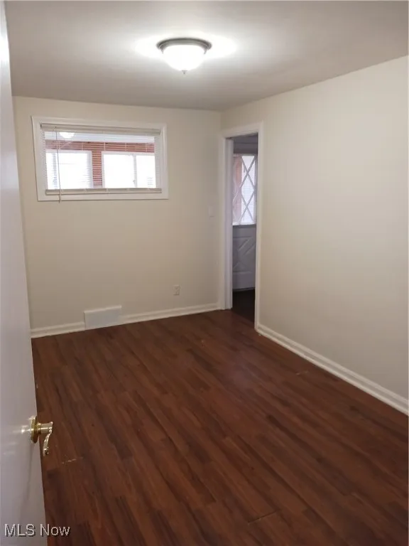 Spare room with dark wood-type flooring and baseboards