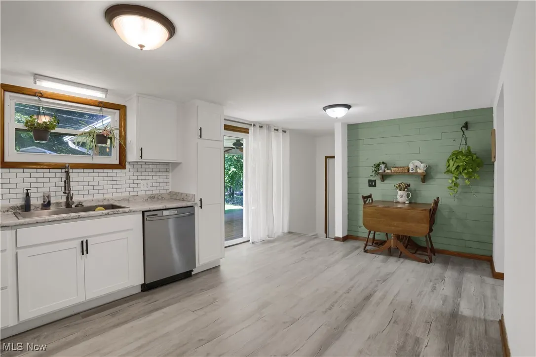 Kitchen with white cabinetry, dishwasher, light wood-style flooring, tasteful backsplash, and wood walls