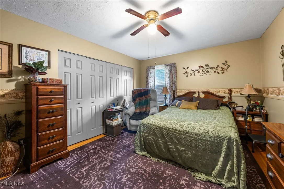 Bedroom with a closet, a textured ceiling, a ceiling fan, and dark wood-type flooring