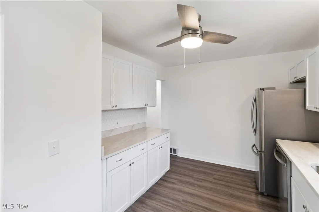 Kitchen with light countertops, dark wood-style flooring, white cabinetry, decorative backsplash, and stainless steel dishwasher