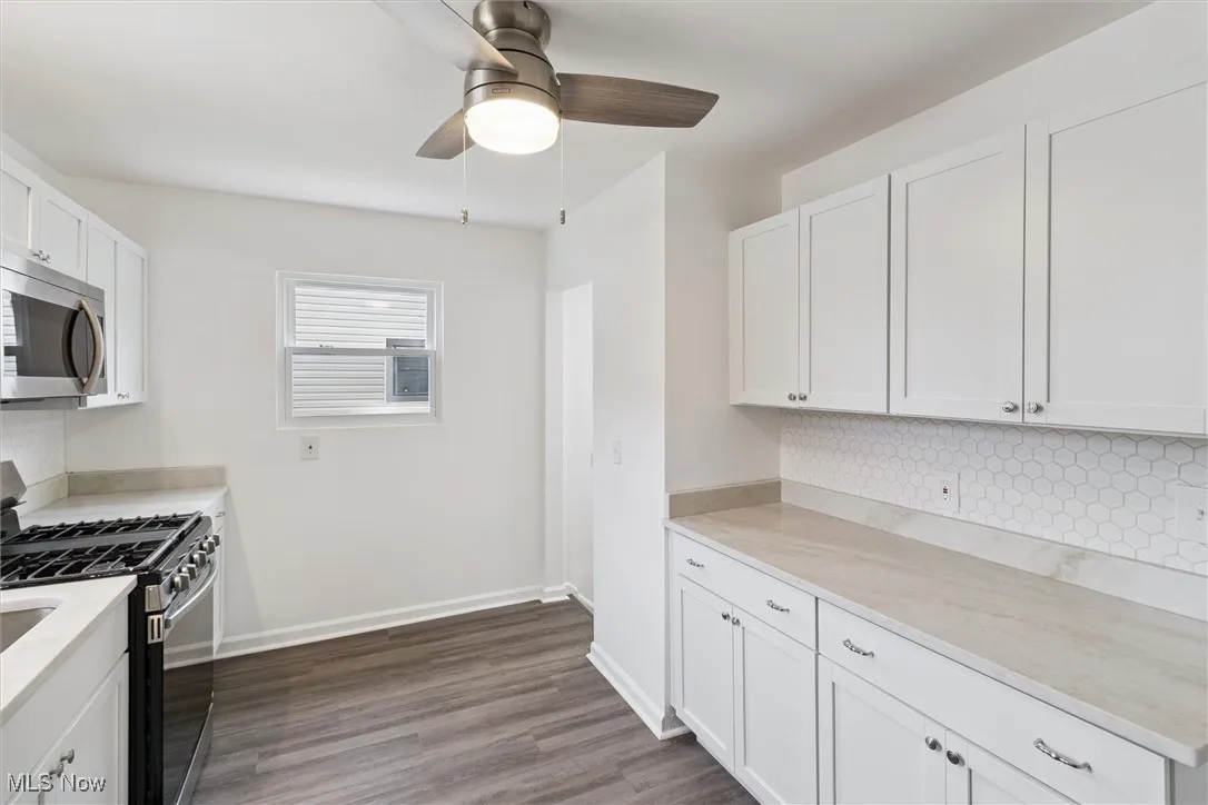 Kitchen with appliances with stainless steel finishes, white cabinetry, tasteful backsplash, dark wood-style floors, and a ceiling fan