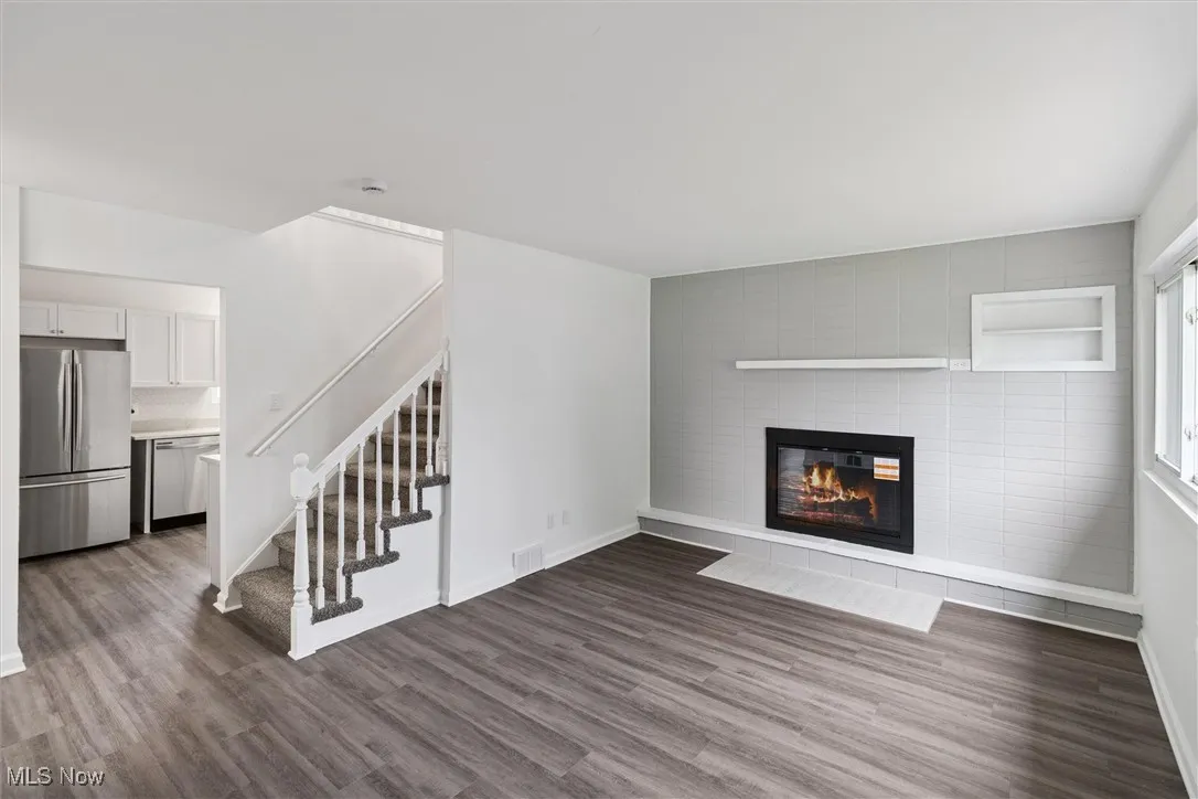 Unfurnished living room featuring stairs, wood finished floors, and a tile fireplace