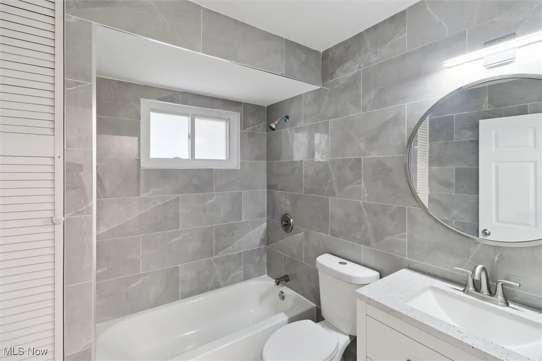 Full bathroom featuring tile walls, shower / tub combination, vanity, and a closet
