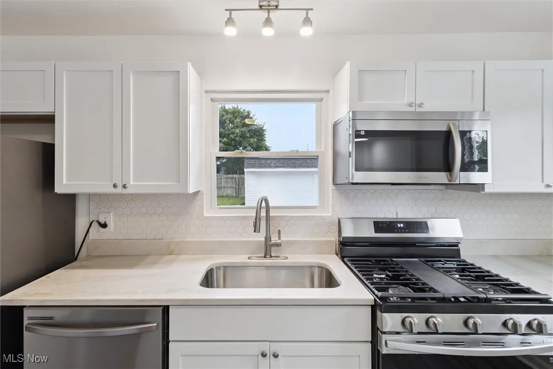 Kitchen with stainless steel appliances, decorative backsplash, white cabinets, and light stone countertops