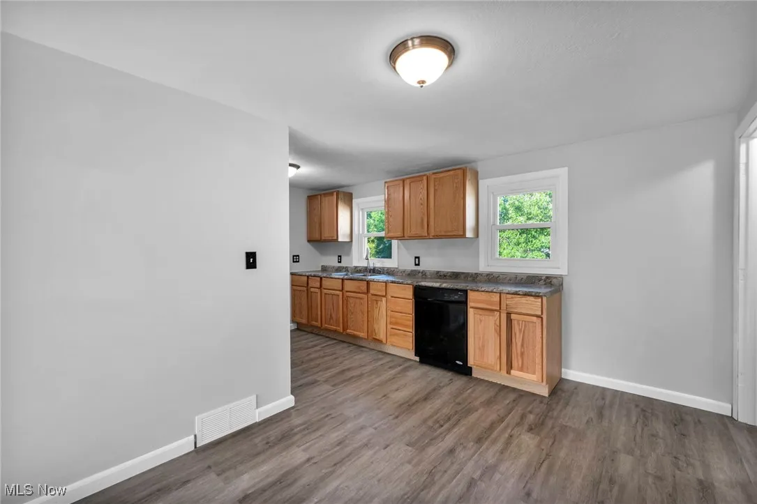 Kitchen featuring dark countertops, brown cabinetry, dark wood-style floors, and dishwasher