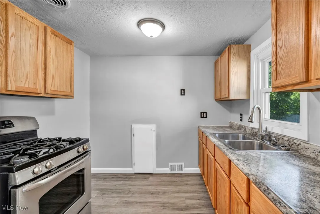 Kitchen with stainless steel gas range, light wood-style floors, a textured ceiling, and light countertops