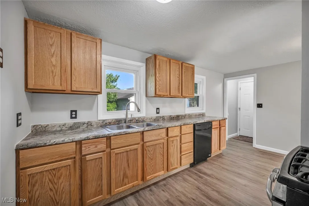 Kitchen with light wood-style flooring, gas range, a textured ceiling, dishwasher, and brown cabinetry