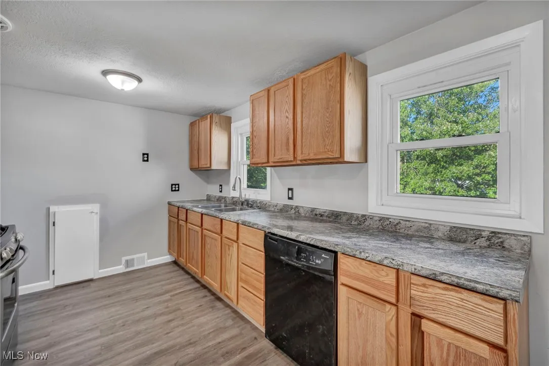 Kitchen with dishwasher, light wood finished floors, stainless steel gas stove, and a textured ceiling