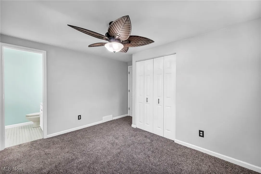 Unfurnished bedroom featuring a closet, carpet flooring, ensuite bathroom, and a ceiling fan