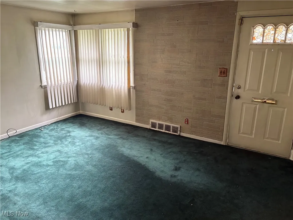 Empty room featuring dark colored carpet and an accent wall