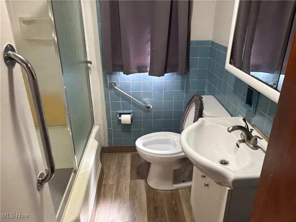 Full bathroom with dark wood finished floors, vanity, tile walls, and enclosed tub / shower combo