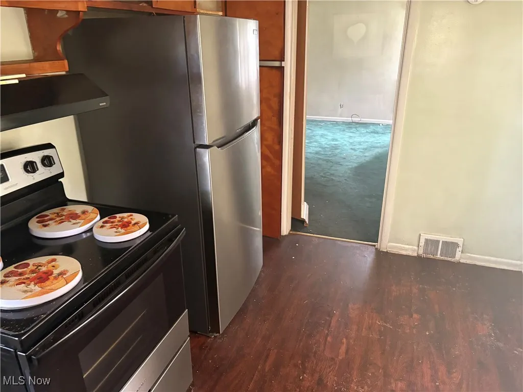 Kitchen featuring electric range, brown cabinets, range hood, dark wood-type flooring, and freestanding refrigerator