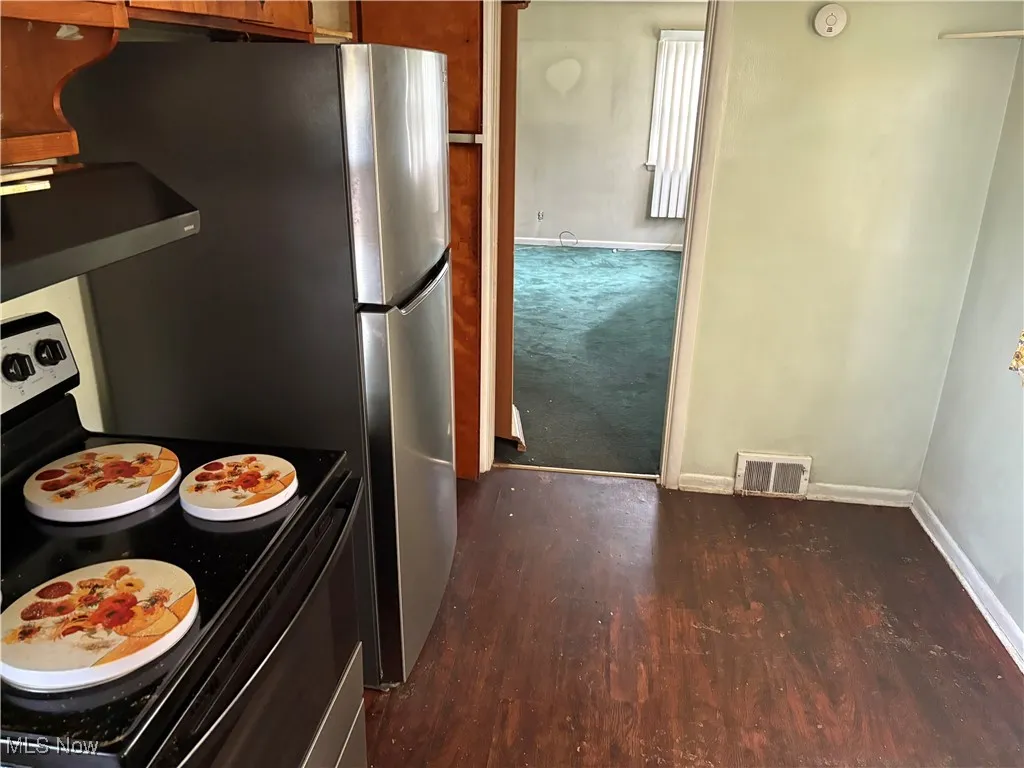 Kitchen with electric range, dark wood-style flooring, extractor fan, and brown cabinetry