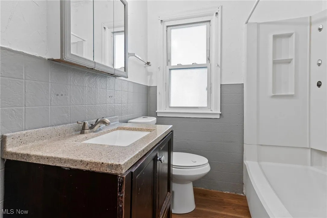 Full bath with dark wood-type flooring, tile walls, vanity, a wainscoted wall, and shower / washtub combination
