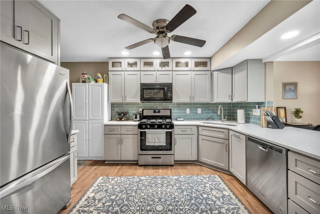 Updated Kitchen with gray cabinetry, appliances with stainless steel finishes, decorative backsplash, recessed lighting, and light wood-style floors throughout