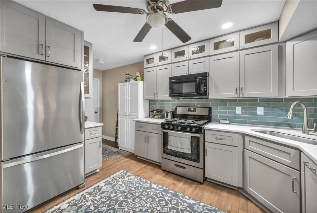 updated Kitchen with gray cabinets, stainless steel appliances, glass insert cabinets, tasteful backsplash, and recessed lighting, ceiling fan
