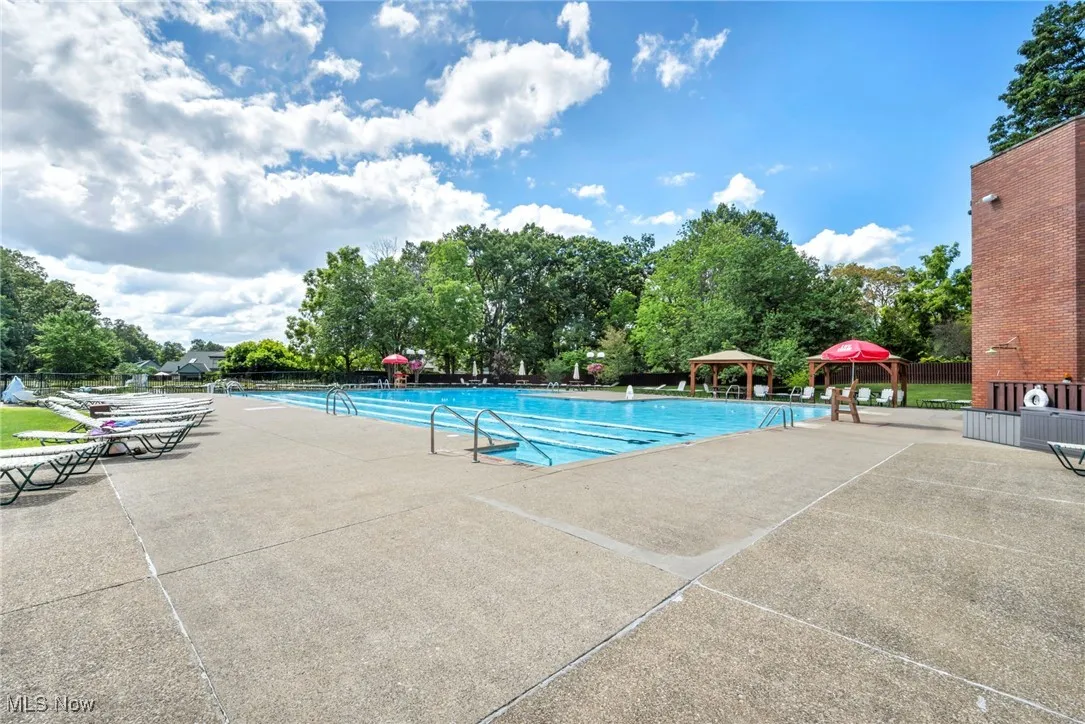 Community pool featuring a patio area, view of scattered trees, and a gazebo