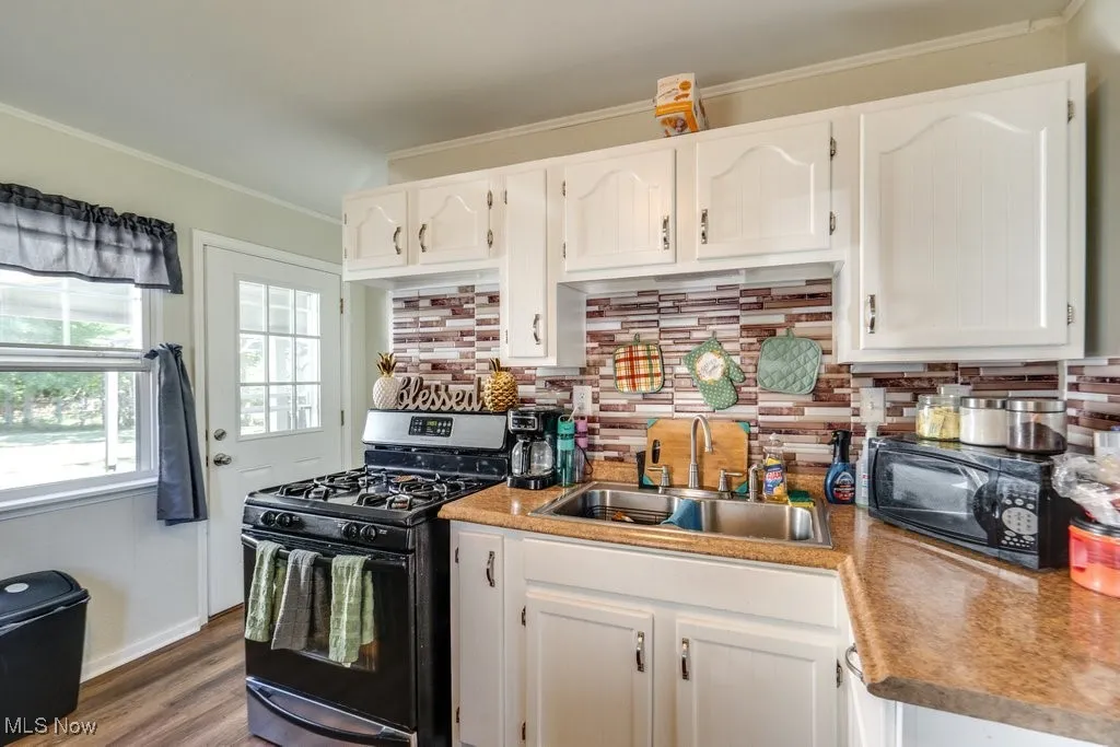 Kitchen featuring range with gas stovetop, crown molding, white cabinetry, tasteful backsplash, and black microwave