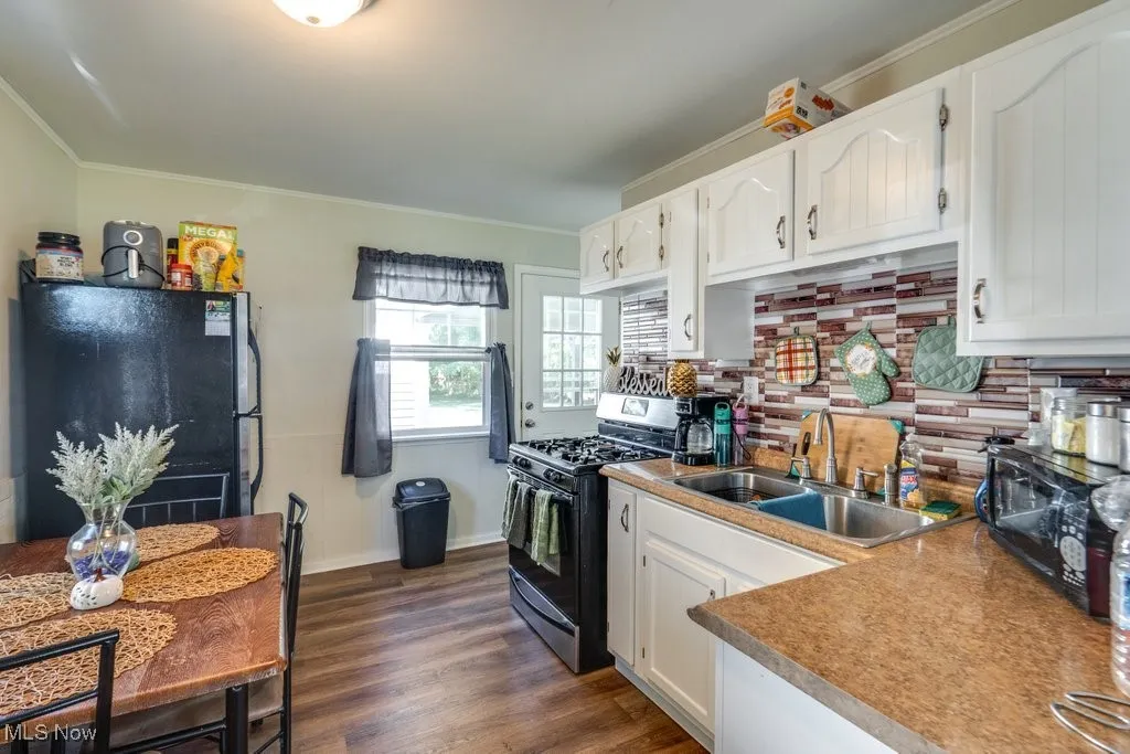 Kitchen with appliances with stainless steel finishes, white cabinetry, ornamental molding, backsplash, and dark wood-type flooring