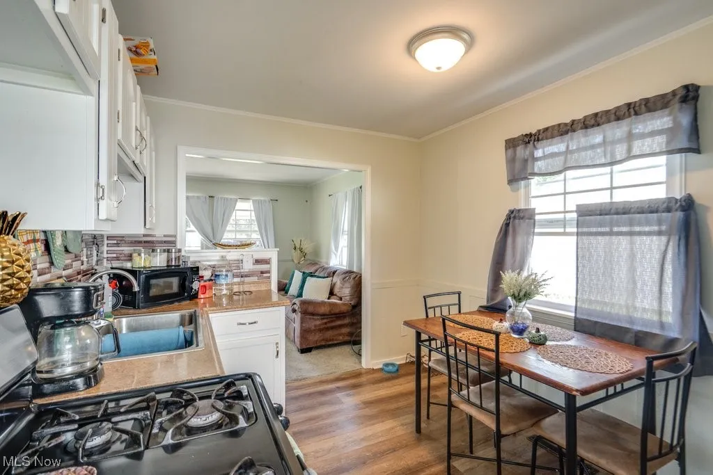 Kitchen with white cabinets, black appliances, crown molding, light wood-style floors, and a wainscoted wall