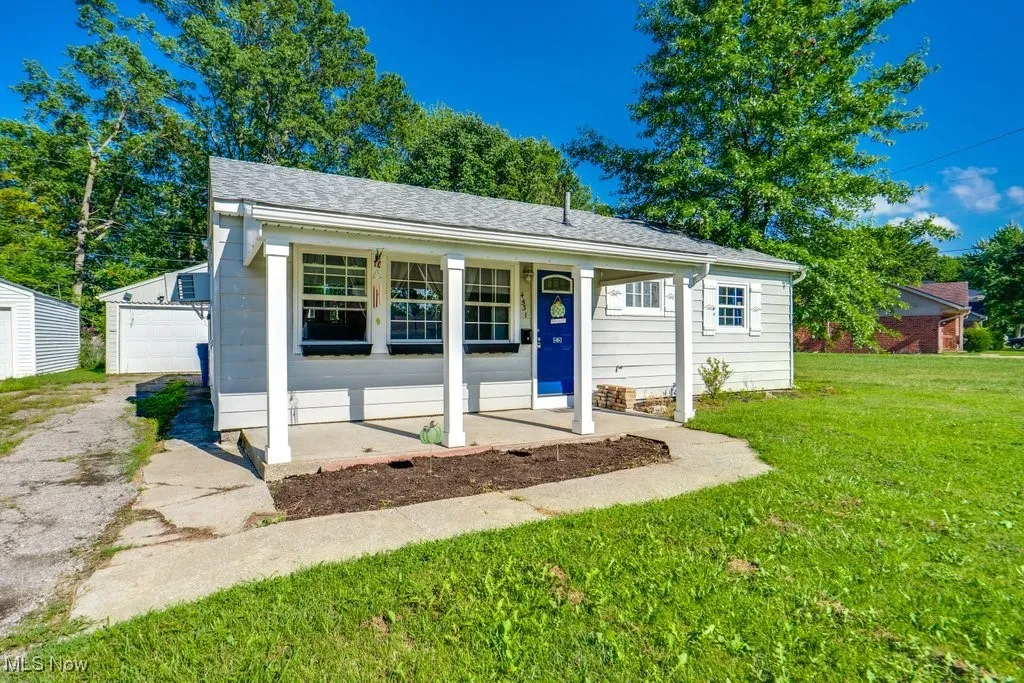 View of front of home featuring covered porch, an outbuilding, a shingled roof, a front yard, and a detached garage