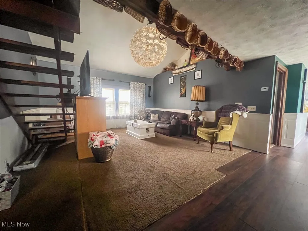 Living room with wood finished floors, a wainscoted wall, a chandelier, and vaulted ceiling