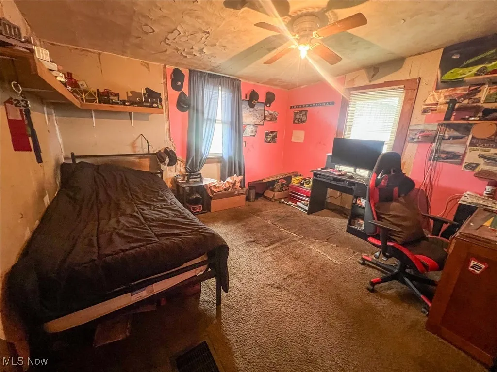 Carpeted bedroom featuring multiple windows, ceiling fan, and a desk
