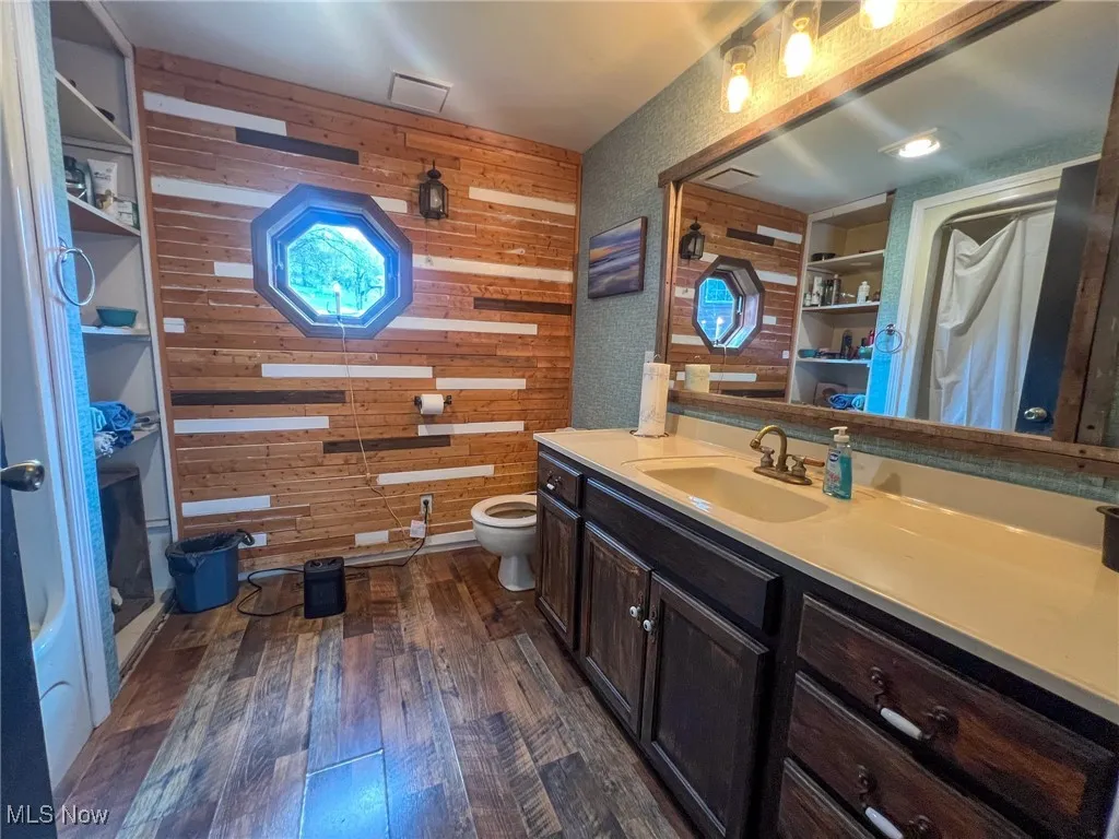 Full bathroom with dark wood-style flooring, vanity, a stall shower, and wood walls