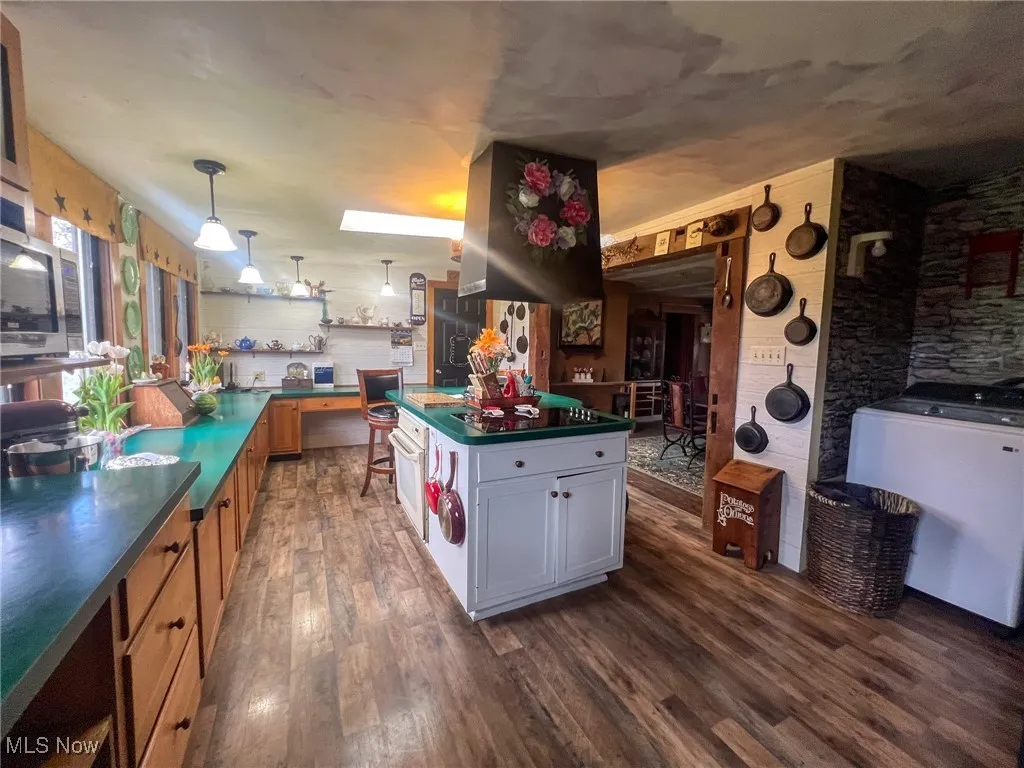 Kitchen with dark countertops, dark wood finished floors, decorative light fixtures, island exhaust hood, and white oven