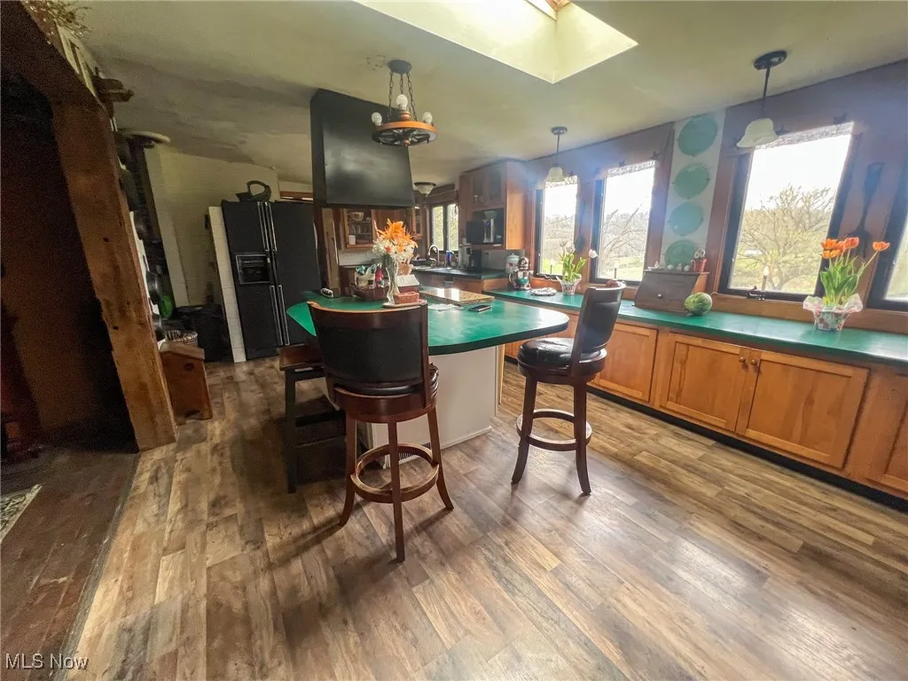 Kitchen with a breakfast bar area, dark countertops, dark wood-type flooring, black fridge with ice dispenser, and brown cabinets
