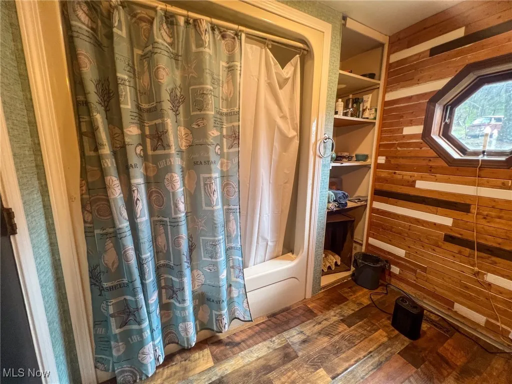 Full bath with wooden walls, dark wood-style floors, and shower / bath combo with shower curtain