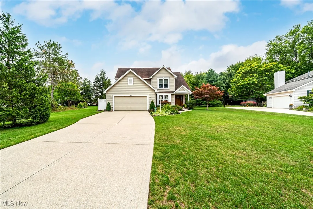Traditional home featuring a front yard, driveway, view of wooded area, and a garage