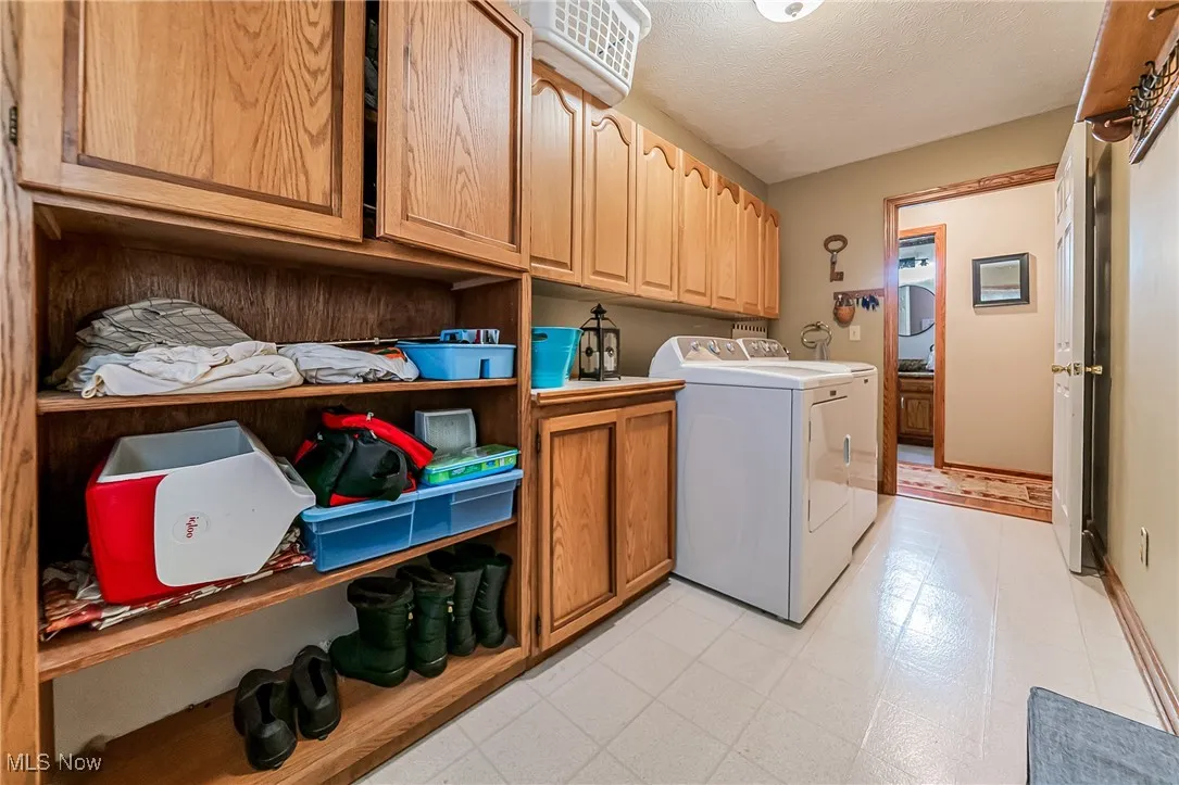 Laundry room with cabinet space, a textured ceiling, light flooring, and washing machine and dryer
