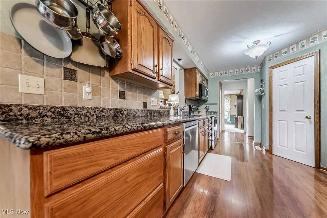 Kitchen featuring brown cabinets, tasteful backsplash, dark wood-type flooring, dark stone counters, and appliances with stainless steel finishes