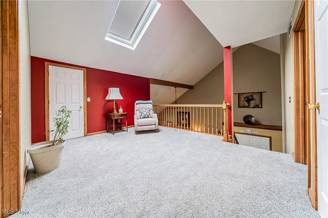Sitting room featuring a skylight, vaulted ceiling, carpet, and an upstairs landing