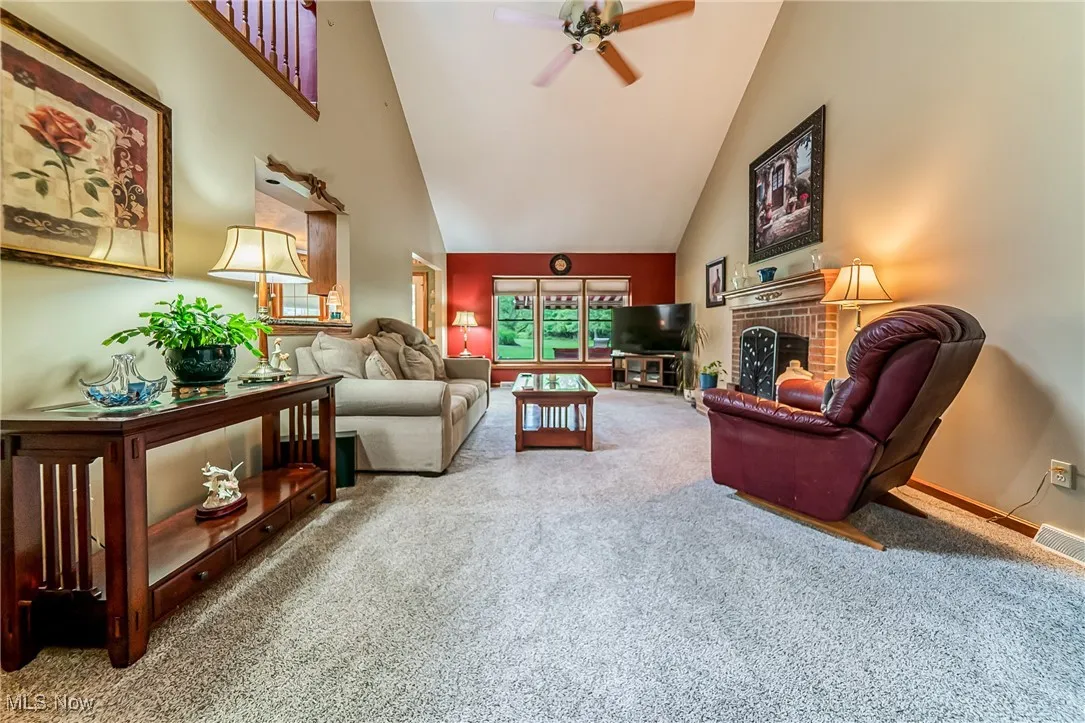 Carpeted living room with high vaulted ceiling, a fireplace, and a ceiling fan