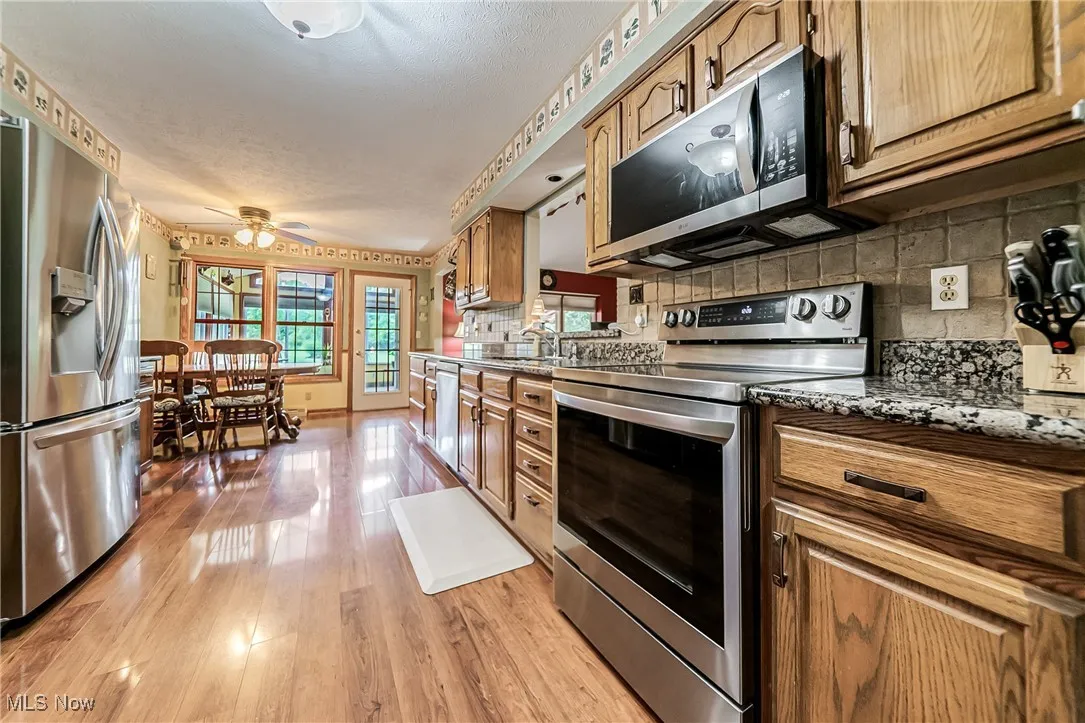 Kitchen featuring stainless steel appliances, ceiling fan, light wood finished floors, decorative backsplash, and brown cabinetry