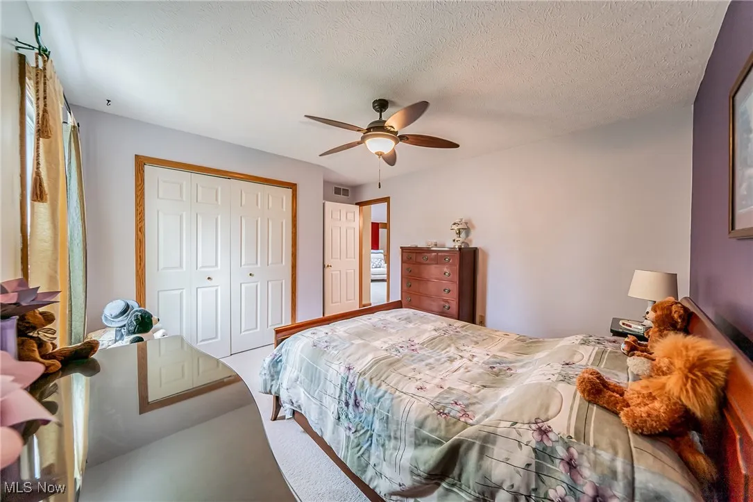 Bedroom with a closet, a ceiling fan, a textured ceiling, and carpet