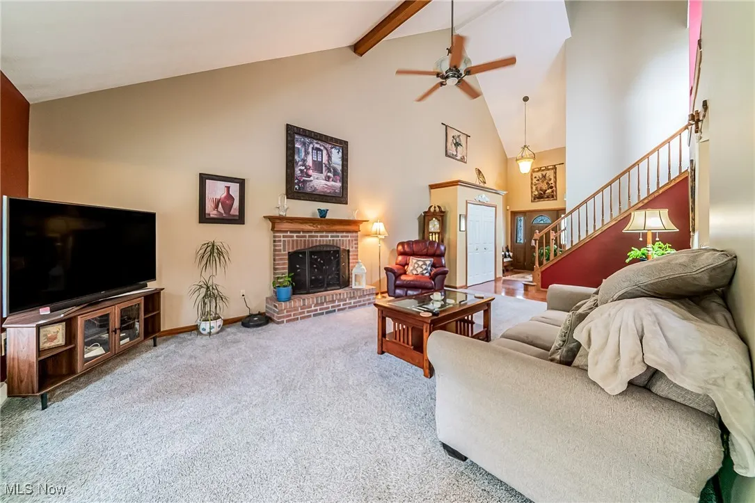 Carpeted living room featuring high vaulted ceiling, beam ceiling, stairway, ceiling fan, and a fireplace