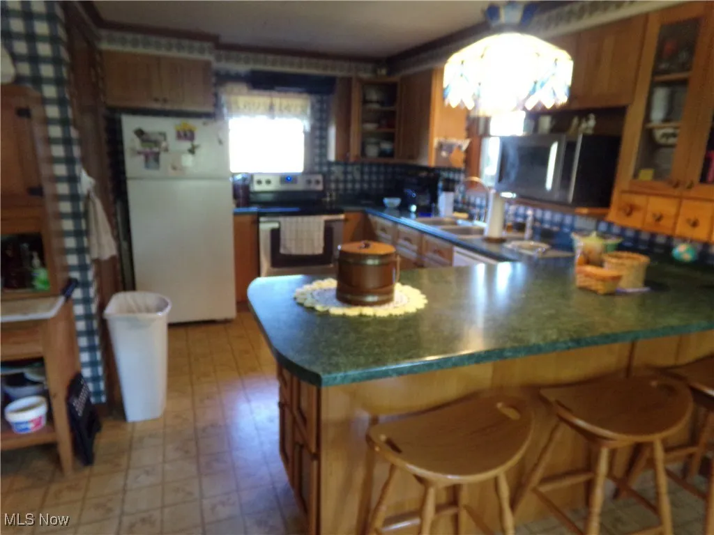 Kitchen with a peninsula, a breakfast bar, stainless steel appliances, glass insert cabinets, and light flooring