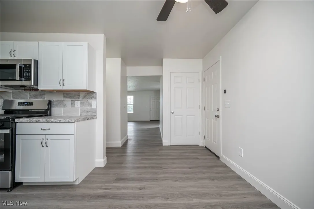 Kitchen with appliances with stainless steel finishes, light wood-style floors, white cabinetry, tasteful backsplash, and light stone counters