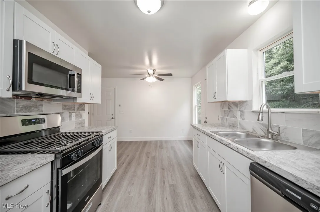 Kitchen featuring decorative backsplash, appliances with stainless steel finishes, white cabinets, and light countertops