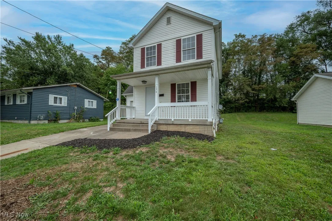 Traditional home featuring covered porch, a front lawn, and view of wooded area