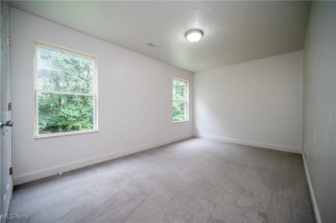 Empty room with light carpet and a textured ceiling