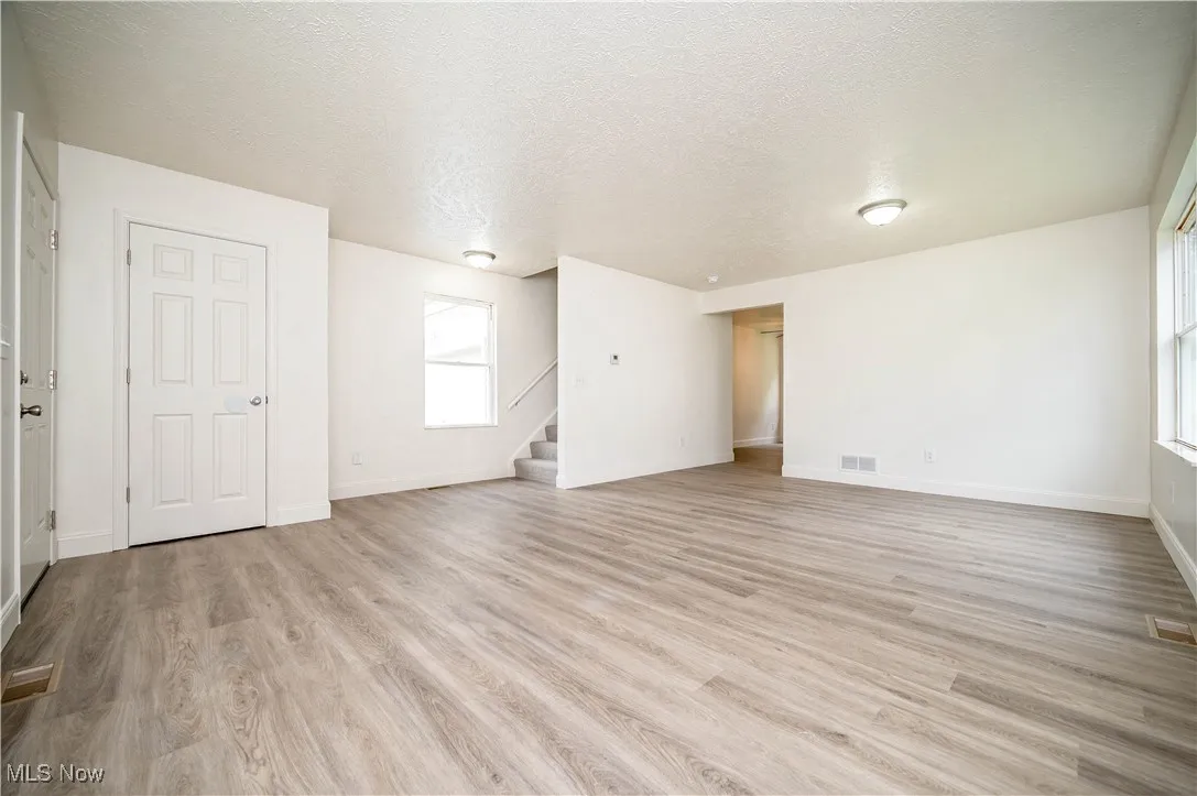 Unfurnished living room with a textured ceiling, light wood-style flooring, and stairs
